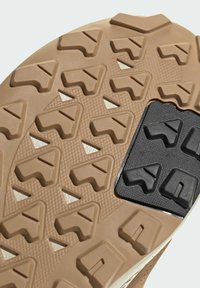 Hellbraune Sneaker-Sohle mit einem strukturierten Muster, dreieckigen Stollen, einem schwarzen Gummieinsatz und einem detaillierten Grip-Design.
