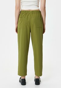 Olijfgroene broek met elastische tailleband, gemaakt van een textuurstof met een gekreukt uiterlijk. Voorzien van twee grote achterzakken en een rechte pijp.