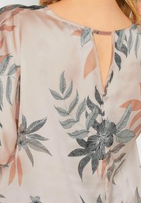 Kukkakuosiset paitapusero, joka on valmistettu kevyestä, silkkisestä kankaasta, jossa on hellä vaaleanpunainen tausta, mustia ja harmaita lehtiä sekä pieni avaus takana.