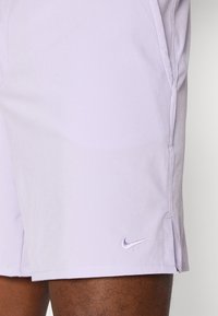 Shorts Nike en lavande clair, fabriqués en tissu léger. Dispose de fentes sur les côtés et d'un petit logo brodé en violet sur la jambe inférieure.