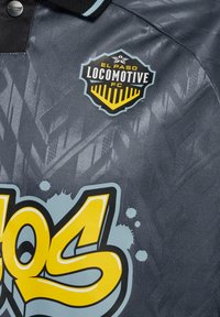 Szary sweter z teksturowanym wzorem, posiadający czarny kołnierz i logo 'El Paso Locomotive FC' w czerni i żółci. Duży żółty detal graficzny.