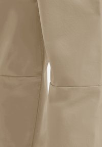 Primo piano di tessuto beige che mostra il dettaglio della cucitura sui pantaloni con enfasi sulla texture e le impunture.