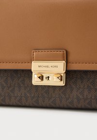 Καφέ δερμάτινη τσάντα με υφή στο σκούρο καφέ κάτω τμήμα. Διαθέτει χρυσό κούμπωμα με το λογότυπο "Michael Kors".