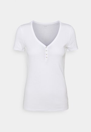 Bílé bavlněné tričko s výstřihem do V, krátkými rukávy a pěti knoflíky na přední straně. Hladká textura, klasický střih.