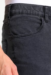 Jeans de mezclilla en un tono oscuro, con un diseño ajustado, que cuentan con bolsillos delanteros y traseros, costuras en contraste y un pequeño detalle de botón metálico.