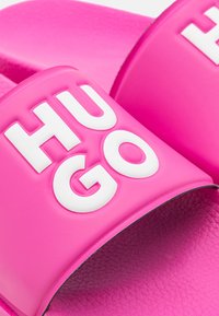 Infradito rosa vivace con grandi lettere bianche in rilievo "HUGO" sulle fasce, che mostrano una texture sulle suole.