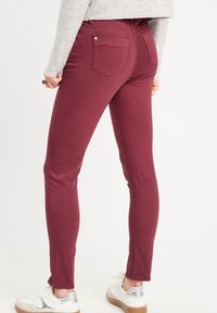 Jean skinny bordeaux avec une texture lisse, dotés de deux poches arrière et d'une coupe ajustée, associés à des baskets blanches.