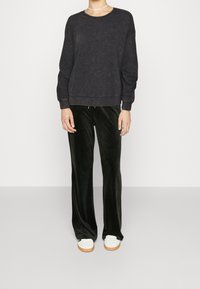 Sudadera gris oscura con cuello redondo y puños acanalados, combinada con pantalones de terciopelo negro y zapatillas blancas con suela clara.