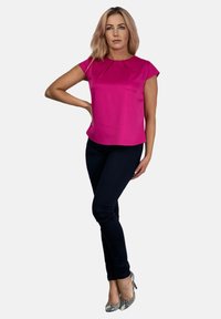 Fuksjowa bluzka z krótkim rękawem z detalem w fałdzie, zestawiona z czarnymi rurkami i srebrnymi szpilkami w wzór węża. Gładki materiał o wyrafinowanej sylwetce.