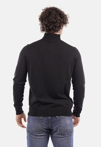 Pullover nero lavorato a maglia con colletto alto, maniche lunghe e orlo a coste. Il retro presenta una texture liscia e un design aderente.