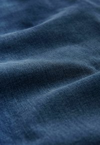 Tmavomodrý denímový materiál s hladkým povrchom, ktorý vykazuje jemné variácie v odtieni a jemné tkané vzory v twill štruktúre po celom povrchu.
