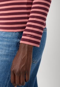 Camicia a maniche lunghe con righe orizzontali color bordeaux e rosa, in tessuto di cotone, con il logo GANT ricamato sul polsino della manica.