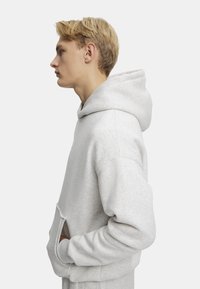 Lys grå hættetrøje, blødt stof, oversized pasform, kængurulomme, ribbet manchetter og kant, med en justerbar hætte med snøre.