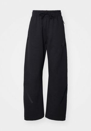 Pantalones de chándal negros con cintura elástica, cordón, dos bolsillos laterales y sutiles acentos de rayas en los laterales. Textura de tela suave.
