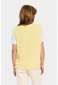 Gult stickat ärmlöst linne med en något lös passform, parat med en vit t-shirt. Mjuk textur och ribbad kantdetalj i botten.