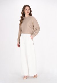 Maglia beige a maniche lunghe con scollo a barca abbinata a pantaloni bianchi a gamba larga con vita alta. Texture morbida, decorazioni minime.