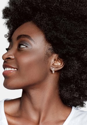 Silver hoopörhänge på en ljusbrun hudton, med texturerad afrohårstil och minimal sminkning, mot en neutral bakgrund.