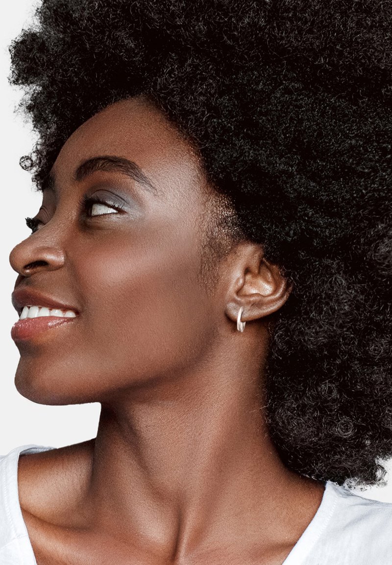 Silver hoopörhänge på en ljusbrun hudton, med texturerad afrohårstil och minimal sminkning, mot en neutral bakgrund.