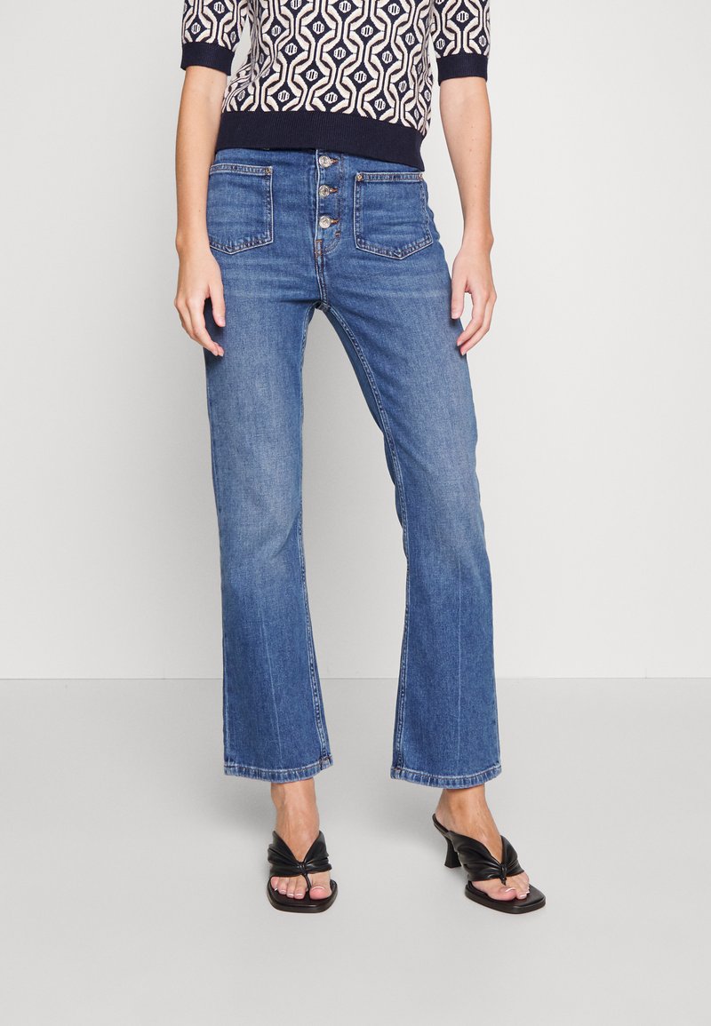Blue denim flared pants with a high waist, featuring five pockets and a button fly. The fabric has a smooth texture and slight stretch.