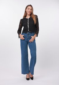 Bluza neagră din dantelă cu mâneci lungi și detalii cu nasturi, asortată cu blugi largi din denim albastru, cu talie înaltă, și pantofi eleganți negri cu toc.