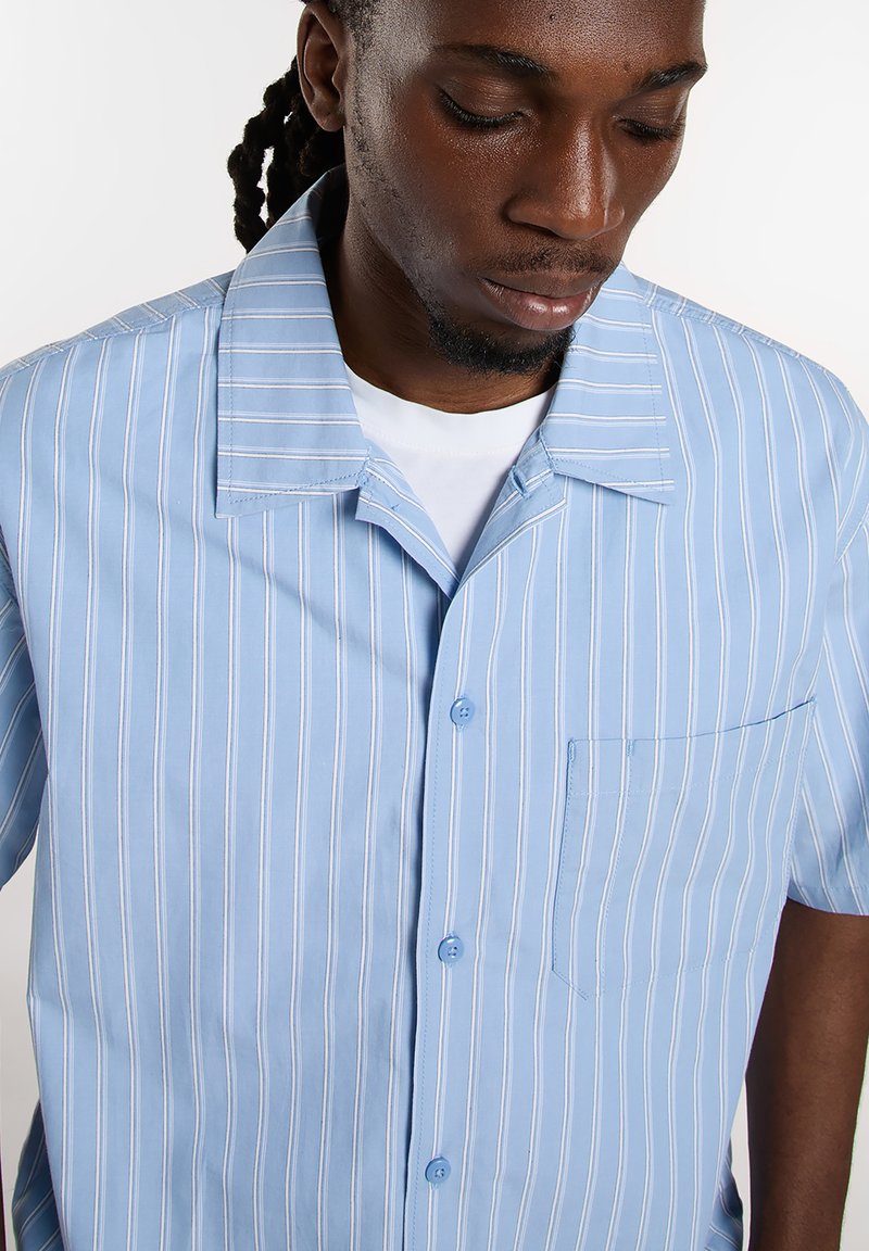 Lyseblå kortærmet skjorte med lodrette hvide striber, knaplukning, spids krave og brystlomme. Glat stoftstruktur.