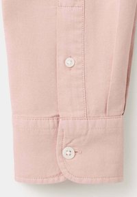 Poignet de manche de chemise rose clair avec deux boutons blancs et une couture visible sur un tissu texturé.