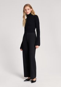 Czarny sweter z golfem o dopasowanym kroju i prążkowanej teksturze, w połączeniu z szerokimi czarnymi spodniami i czarnymi czółenkami w szpic.