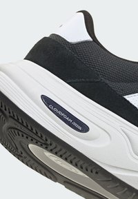 Gros plan d'une chaussure de sport noire et blanche avec une semelle texturée et une étiquette « Cloudfoam Cushion » sur la semelle intermédiaire blanche coussinée.