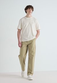 Tricou alb din bumbac, cu mâneci scurte, asortat cu pantaloni lejeri de culoare khaki. Adidași albi completează ținuta. Design simplu, fără modele.