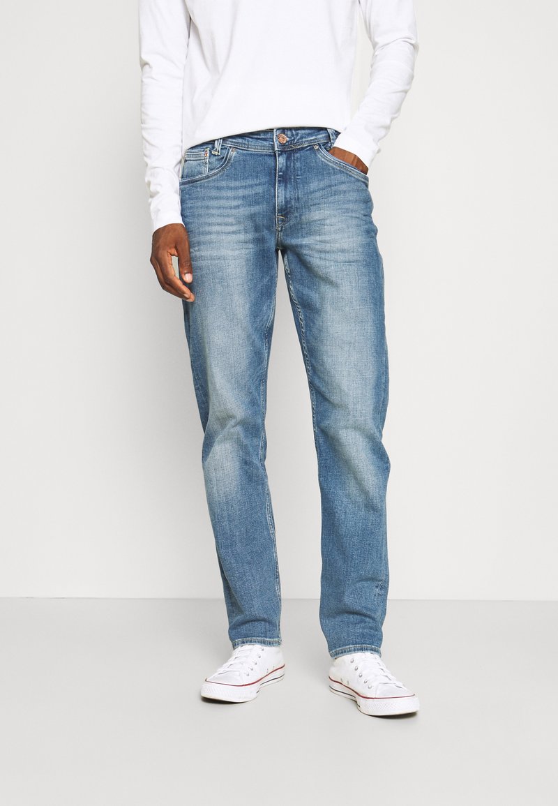 Lichtblauwe denim jeans voor heren met een rechte pasvorm, lichte slijtage, vijf zakken en een knoop- en ritsluiting. Gemaakt met witte sneakers.