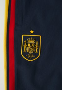 Jūras spēku sporta apģērbs ar zelta zīmi ar kroņu un zvaigzni, sarežģītiem rakstiem un sarkaniem, dzelteniem un melniem svītrainiem akcentiem.