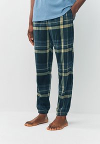 Flanell-Schlafanzughosen in Dunkelgrün mit einem karierten Muster in Gelb und Blau. Elastische Bündchen an den Knöcheln und eine lockere Passform. Weicher Stoff.