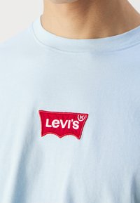 Světle modré bavlněné tričko s červeně vyšitým logem Levi's v klasickém tvaru batwing, se hladkou texturou a kulatým výstřihem.