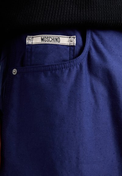 Marinblå tygbyxor med Moschino-märke på bakfickan, med kontrasterande sömnad och detalj av en silverknapp.