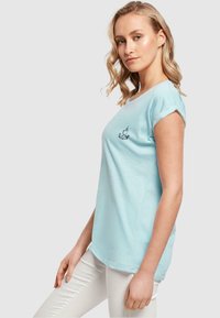 Lys blå T-shirt med korte, rullede ærmer, prydet med et broderet logo på fronten. Fremstillet af blødt, letvægtigt stof med en afslappet pasform.