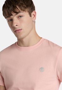 Lichtroze katoenen T-shirt met een ronde halslijn en korte mouwen, met een klein groen geborduurd logo op de borst.
