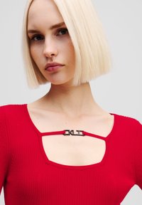 Top roșu cu nervuri, cu decolteu pătrat, bretele subțiri și un detaliu decorativ din metal negru la piept.