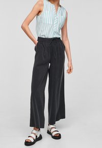 Top manica scoperta a righe azzurre e bianche con scollo a V, due tasche sul petto; pantaloni neri a gamba larga con vita elastica; sandali bianchi.