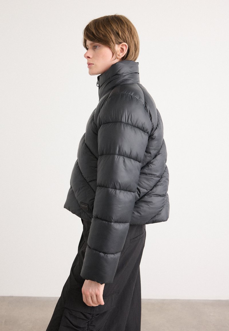 Casaco de puffer em preto com colarinho alto, design matelassé e um corte cropped. Apresenta uma textura suave e detalhe de logotipo nas laterais.