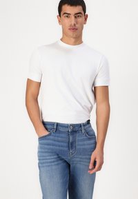 Tricou alb cu mânecă scurtă, fabricat din bumbac, purtat împreună cu blugi din denim de un albastru mediu, cu un croi clasic și o ușoară decolorare.