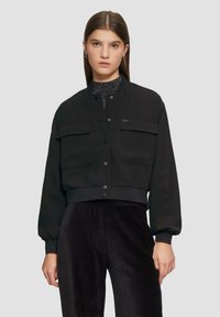 Czarna krótka kurtka z dwoma kieszeniami na piersiach, zapięciem na guziki oraz prążkowanymi mankietami. Wykonana z gładkiego materiału, charakteryzująca się minimalistycznym wzornictwem.