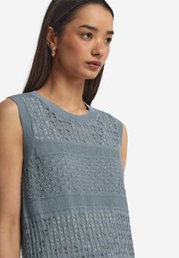 Ljusblå ärmlös topp med intrikata stickade mönster, texturerade band och rund halsringning. Slät yta med öppna vävdetaljer.