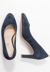 Laivastonsiniset mokkanahka korkokengät, joissa on sileä pinta, terävä kärki ja vaatimaton loivakorko. Sisällä on pehmeä beige pohjallinen.