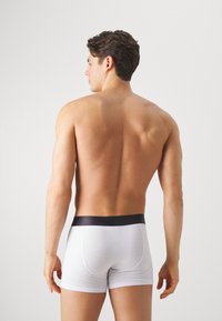 Weiße Baumwoll-Boxershorts mit einem schwarzen elastischen Bund, figurbetontem Design, glatter Textur und ohne sichtbare Muster. Sicht von hinten.