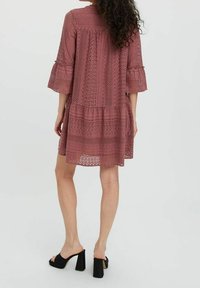 Robe en dentelle couleur framboise avec une coupe en étagères, des manches cloche à trois-quarts et un motif texturé, assortie à des sandales noires à talons carrés.