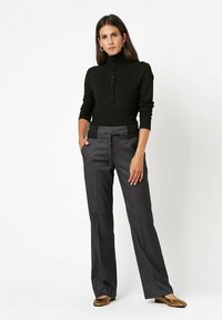 Black ribbed long-sleeve top with button detailing paired with dark gray wide-leg trousers featuring drawstring and pocket accents. Bronze flats.