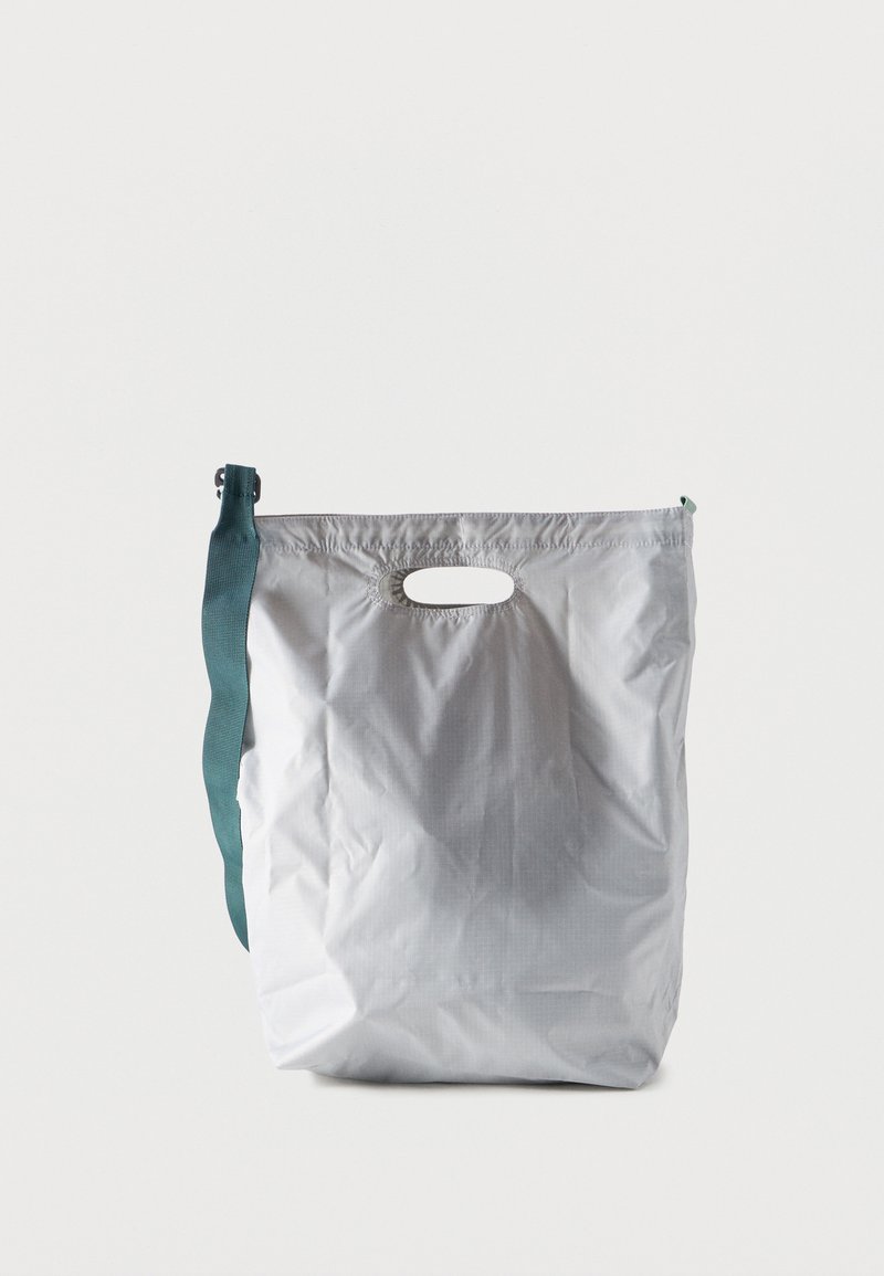 Ανοιχτό γκρι επαναχρησιμοποιήσιμη τσάντα αγορών με λαβή κοπής και σκούρο τιρκουάζ ρυθμιζόμενο λουρί ώμου σε λευκό φόντο.