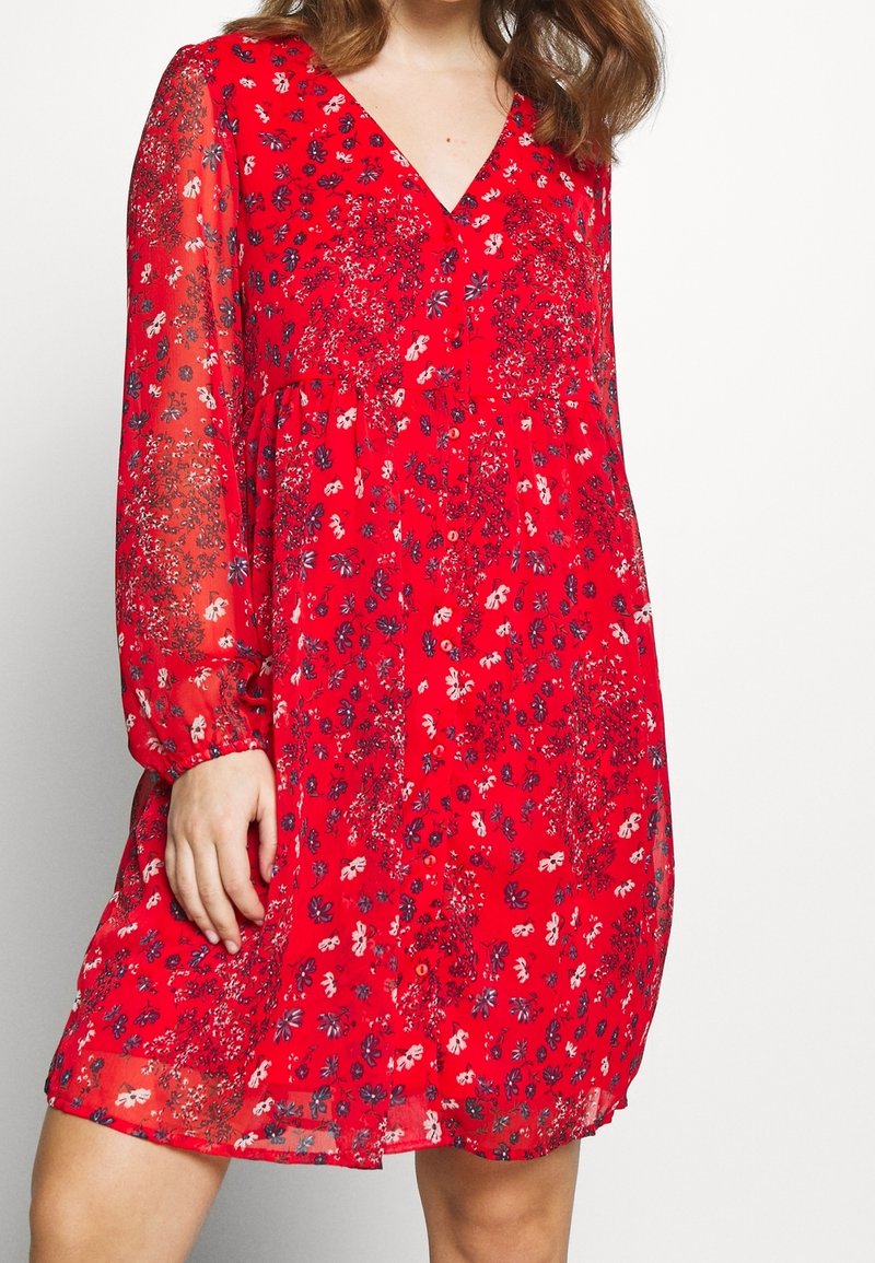 Rotes Blumen Kleid mit langen durchsichtigen Ärmeln, einem V-Ausschnitt und lockerer Passform. Der Stoff hat eine leichte, weiche Textur mit kontrastierenden Mustern.
