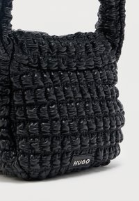 Μαύρη τσάντα χειρός με ρυτιδωτή υφή, κοντή λαβή και μικρό ορθογώνιο λογότυπο Hugo στη κάτω εμπρόσθια γωνία.