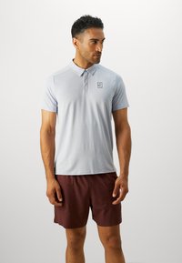 Lyseblå kortærmet polo shirt med krave og et lille logo på brystet, sammen med mørkerøde shorts. Glat tekstur og skræddersyet pasform.